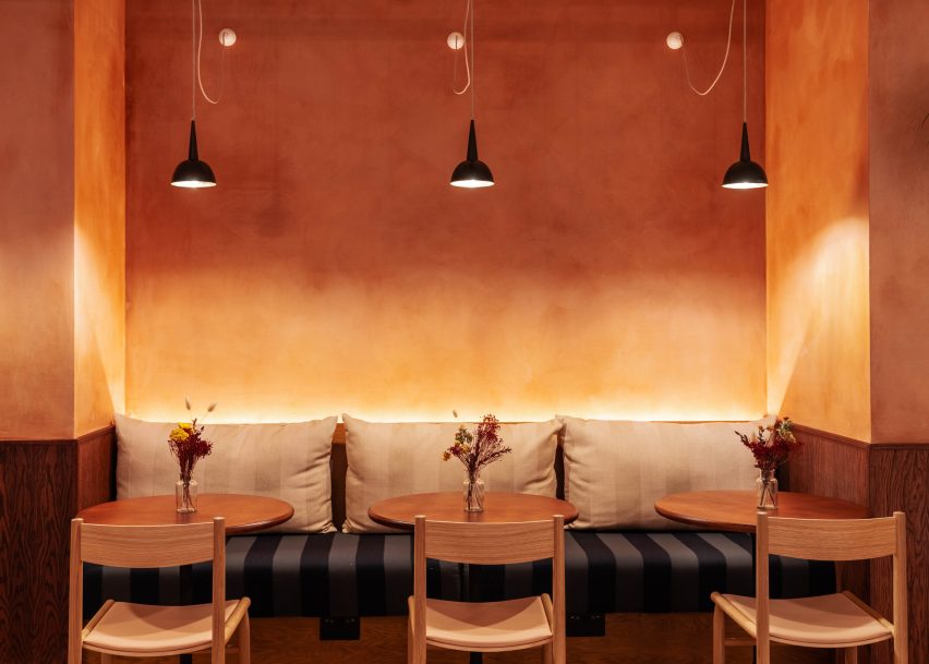 فضای داخلی رستوران با دیوار نارنجی رنگ، چراغ های آویز مشکی، نیمکت و میز و صندلی های چوبی