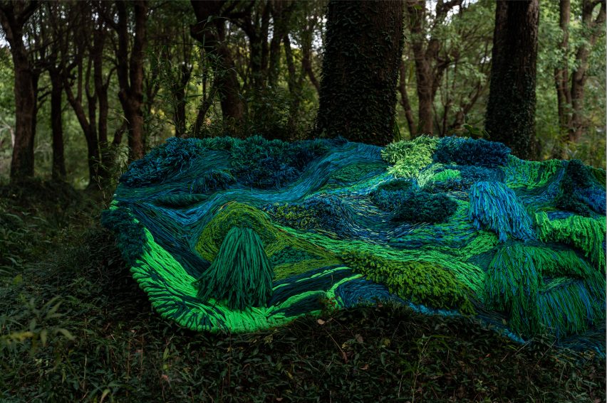 Photo of a green and blue woven design installation on a forest floor