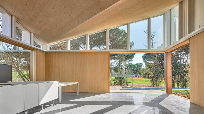 Interior of a mono-pitched timber house with concrete floors and large openings leading to a garden