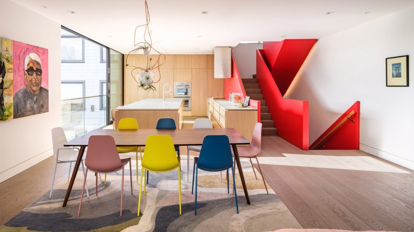 Open-plan kitchen and dining room with colourful chairs, wood units and a red staircase