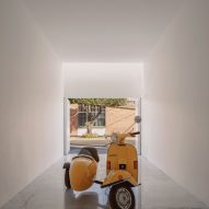 A white square garage with polished concrete floors and a yellow Vespa