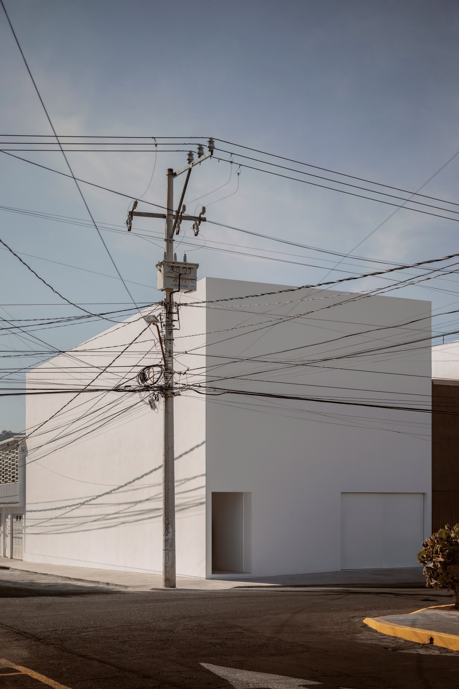 A white cube house on a street corner with telephone poles