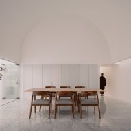 A white dining room with arched ceiling, wooden dining table and chairs, built-in white wall storage and sliding glass doors opening to a courtyard