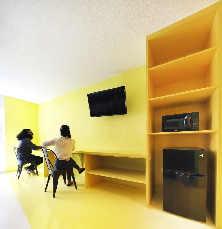 Желто-белый интерьер с желтыми стеллажами вдоль стены и настенным телевизором