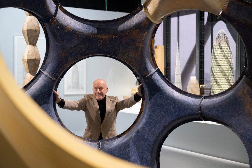 نورمن فاستر در نمایشگاه خود در مرکز پمپیدو از سوراخ دایره ای در یک ساختار مجسمه ای بزرگ نگاه می کند.