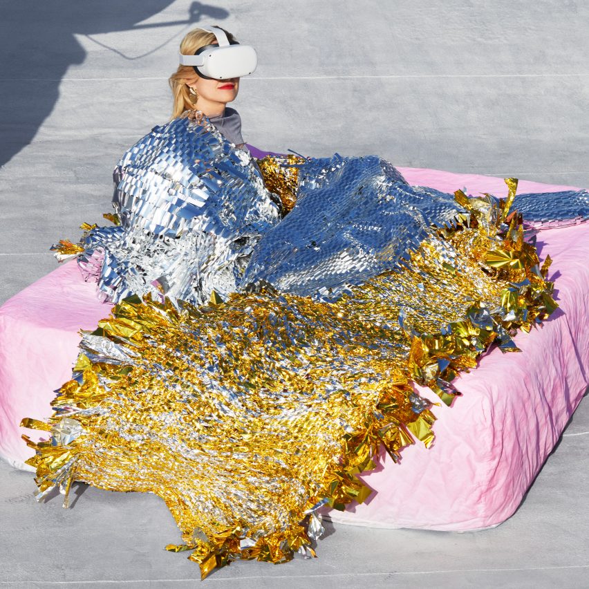 Model sitting on mattress wearing and covered in shiny metallic materials