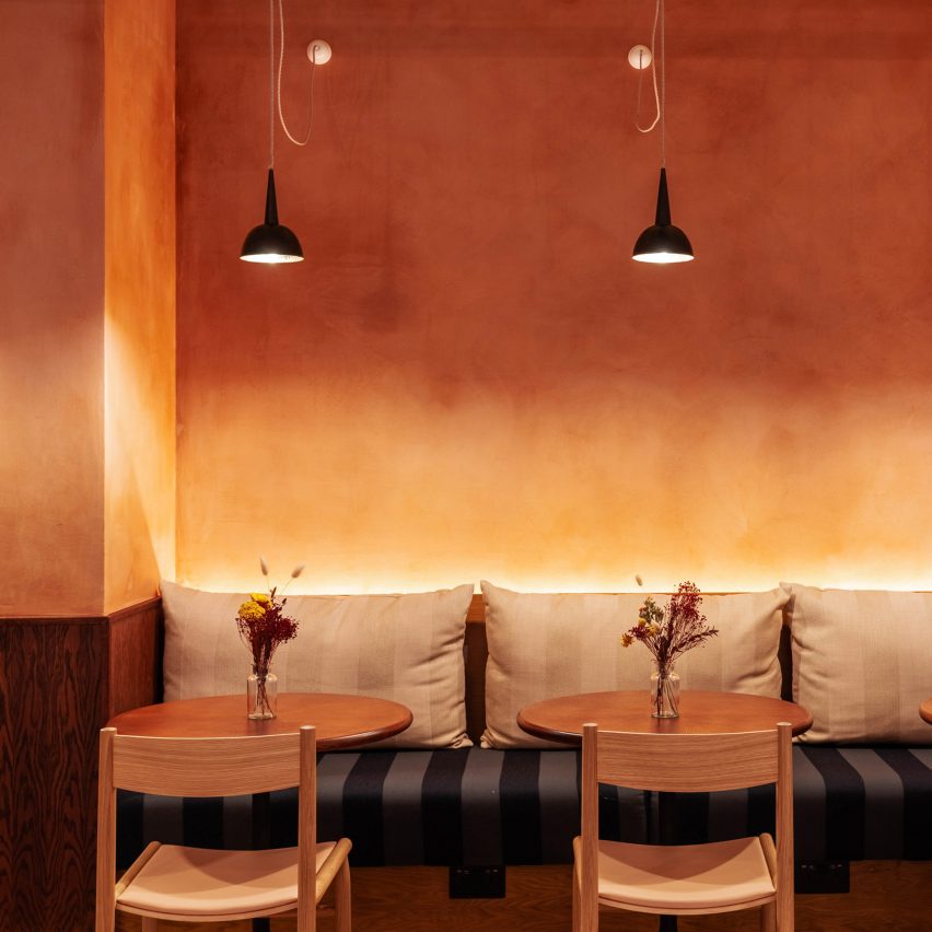 Restaurant interior with an orange ombre wall, black pendant lights, bench seating and wooden tables and chairs