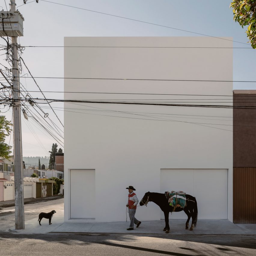 Exterior de una casa cúbica blanca de HW Studio Arquitectos con un hombre, un caballo y un perro al frente
