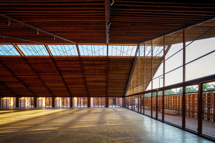 Um amplo espaço interior com um grande telhado inclinado de madeira e uma fachada de vidro