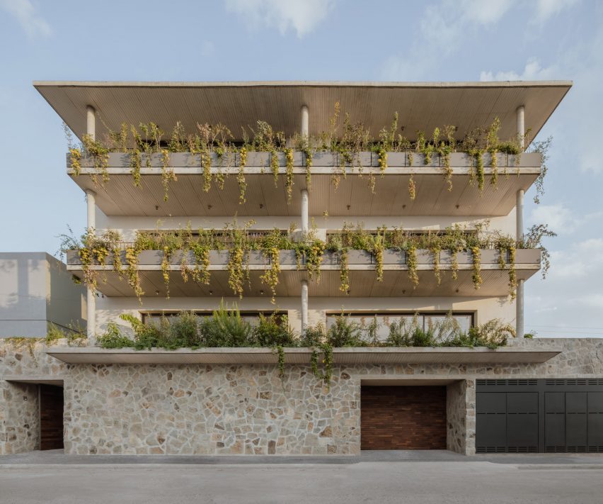 A four-storey apartment building in Mexico with a stone wall and planted balconies