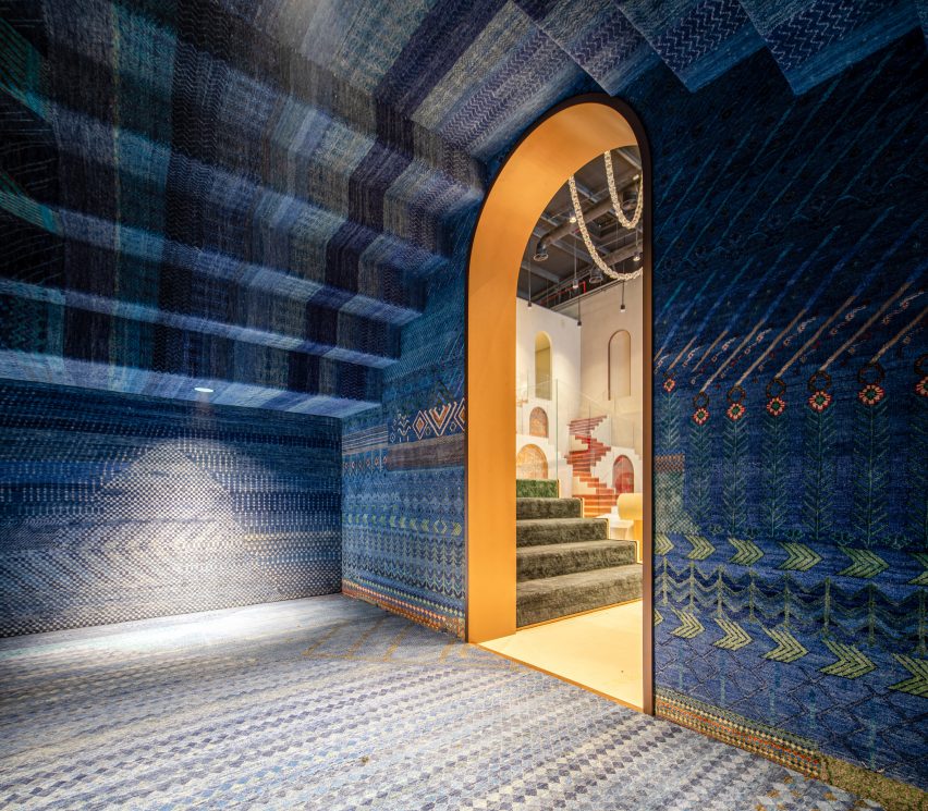 Foto de la sala Sapphire en la sala de exhibición de Dubai de Jaipur Rugs que muestra alfombras azules estampadas que cubren las paredes, el piso y el techo, que también tiene una forma escalonada