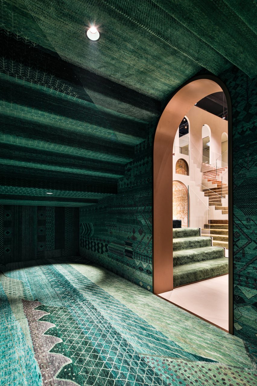 Foto de la Sala Esmeralda en la sala de exhibición de Dubái que muestra alfombras con diseños intrincados de color verde esmeralda del piso al techo y una entrada arqueada que enmarca la tienda más allá