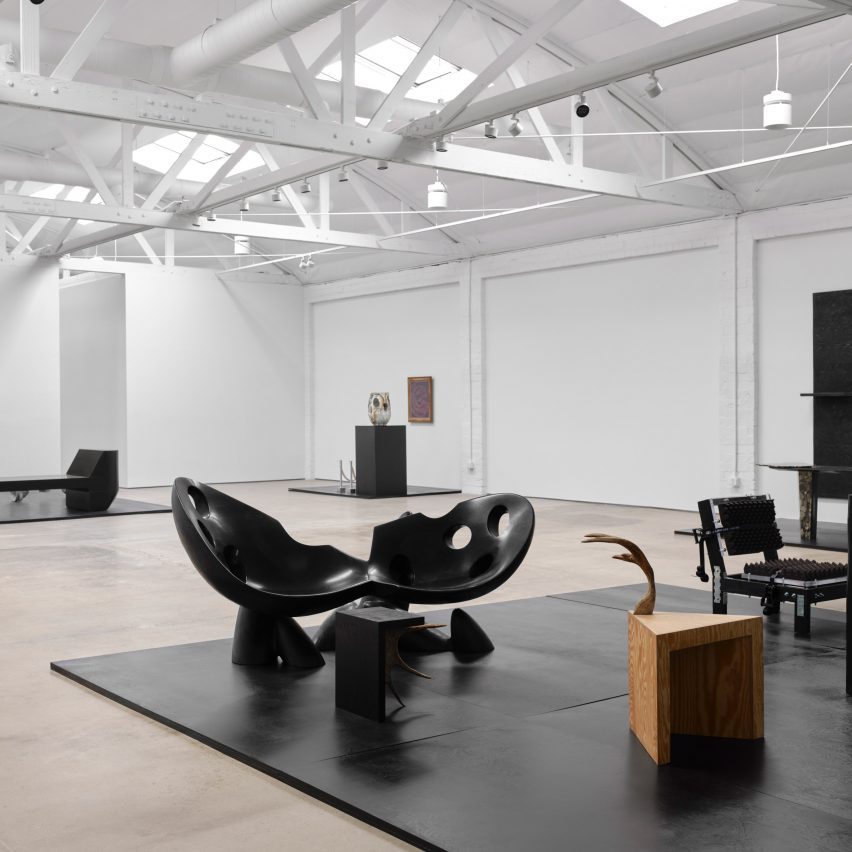 Dark furniture in stark white gallery with trusses on the ceiling