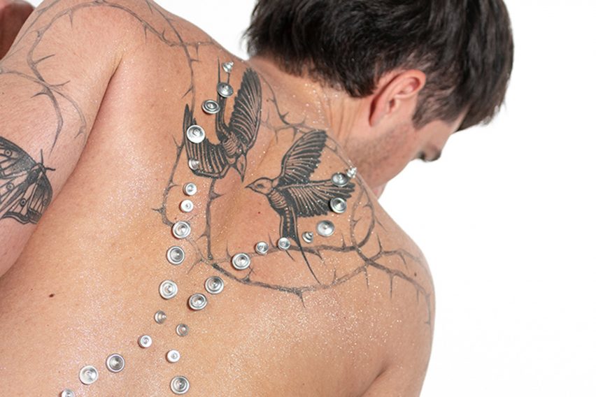 Gemas de plata colocadas en forma de X en la espalda de un modelo tatuado
