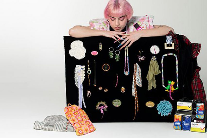 Person with pink hair standing over a black board displaying jewellery by Lucerne School of Art and Design student