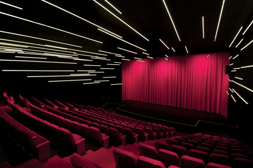 Espacio de teatro con paredes y techos negros, tiras de luces y asientos de color rosa fuerte