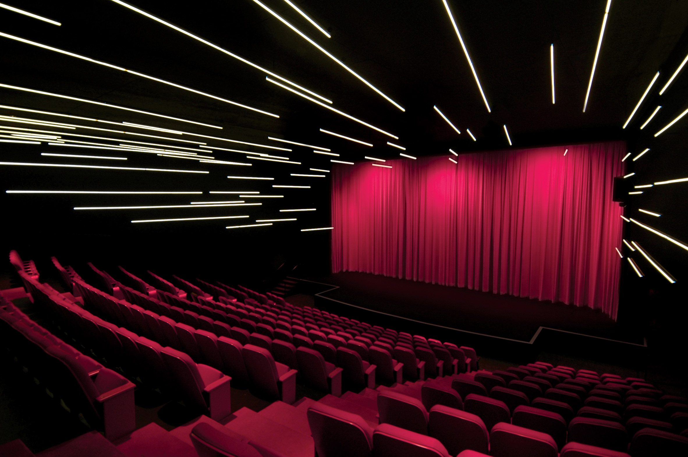 Theatre space with black walls and ceilings, strip lighting and hot pink seats