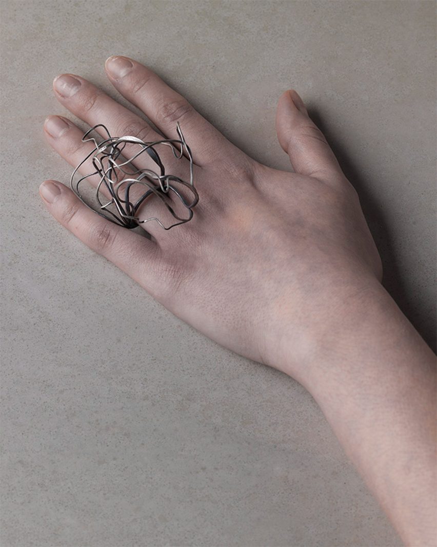 Photograph of a hand wearing a silver ring with an oversized swirling structure
