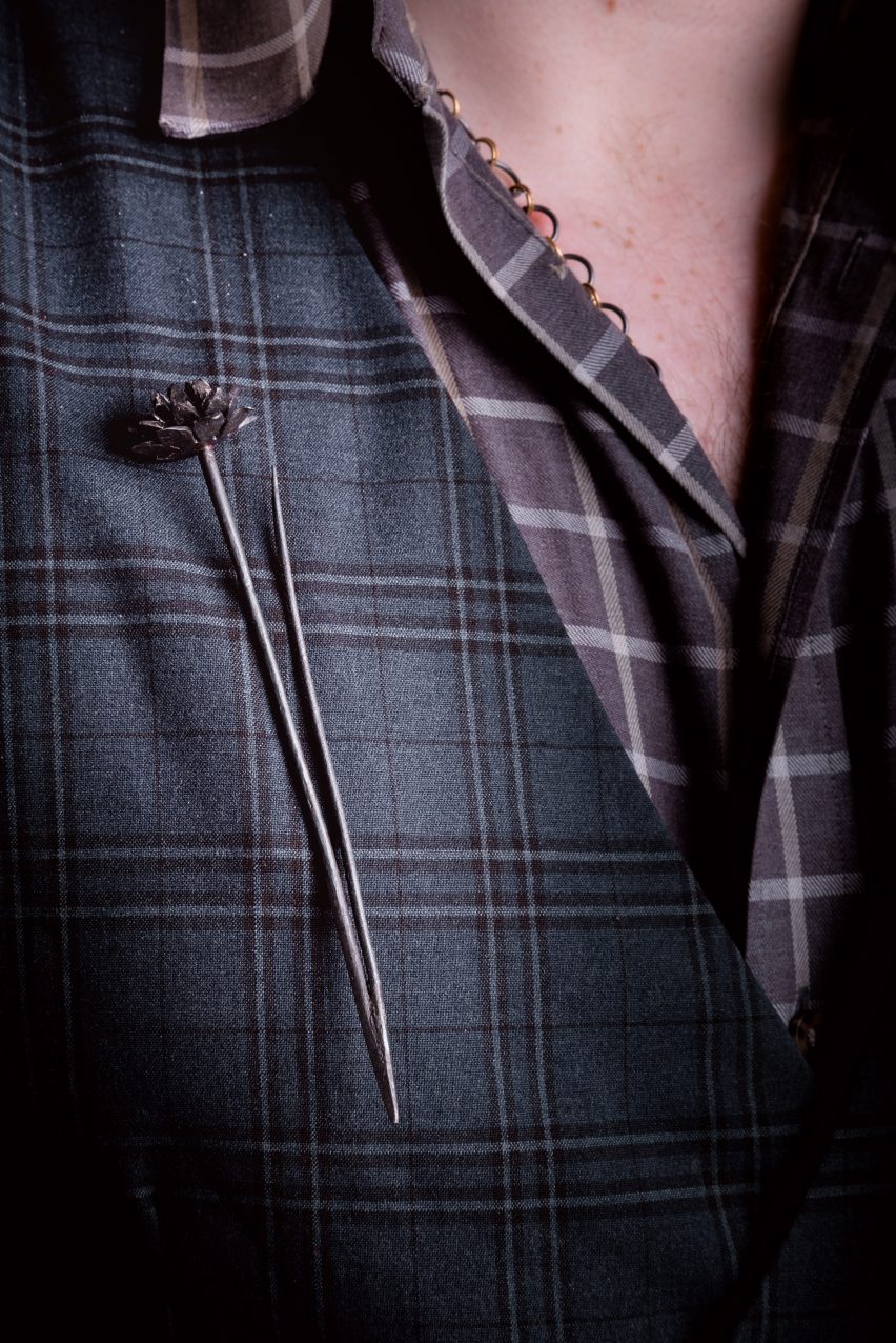 A dark grey pin with a floral head worn on a blue tartan blazer