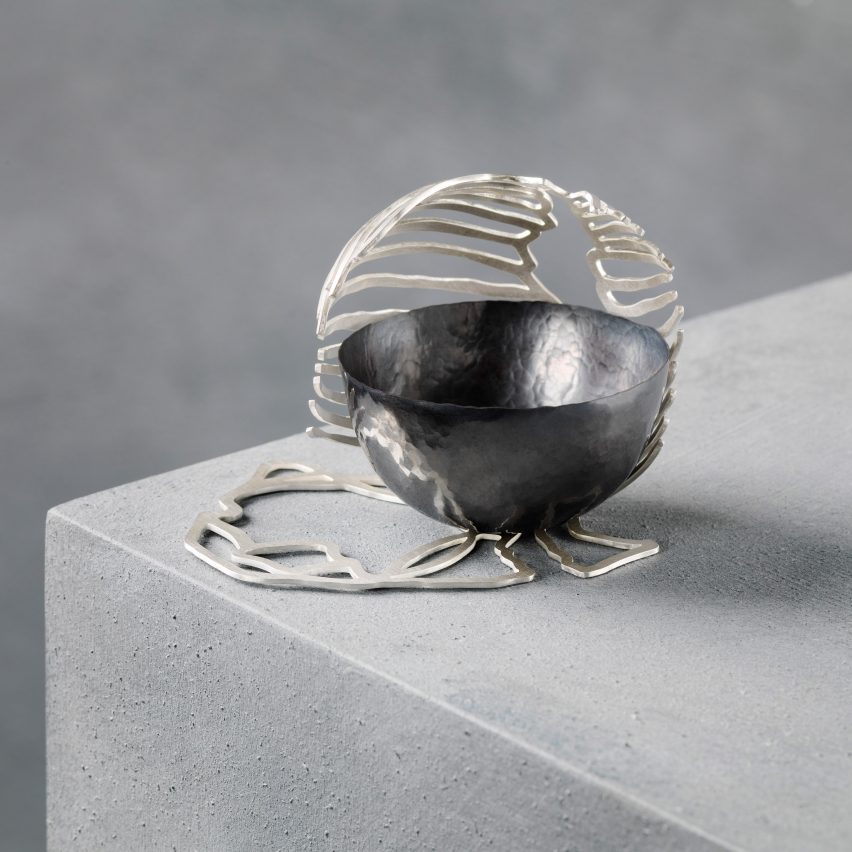 A hemispherical metal bowl on a concrete plinth with a sculptural metal surround