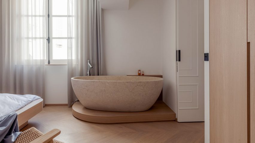 Stone freestanding bathtub on a wooden plinth in a bedroom