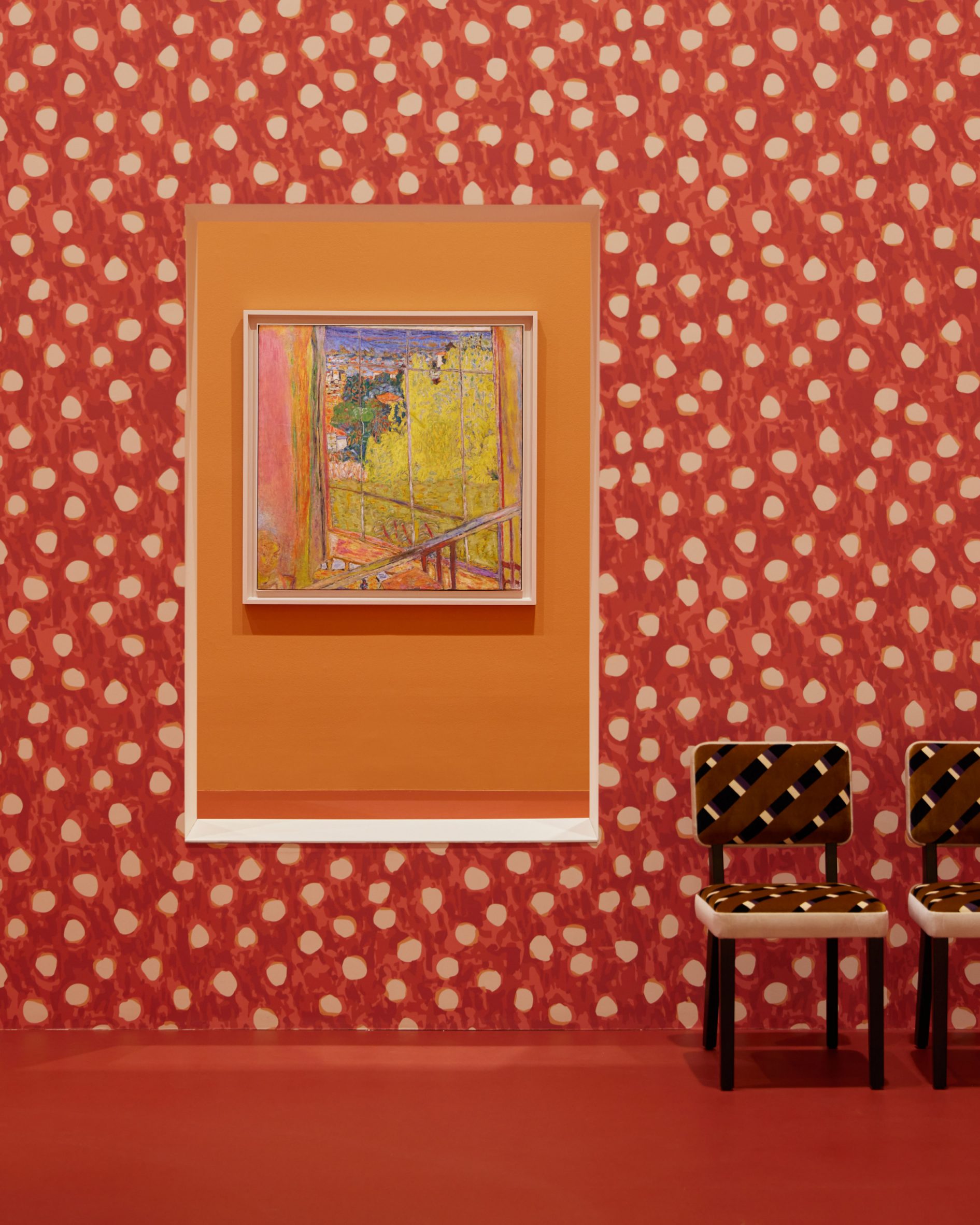 Red wall with white spots frames a painting through an opening