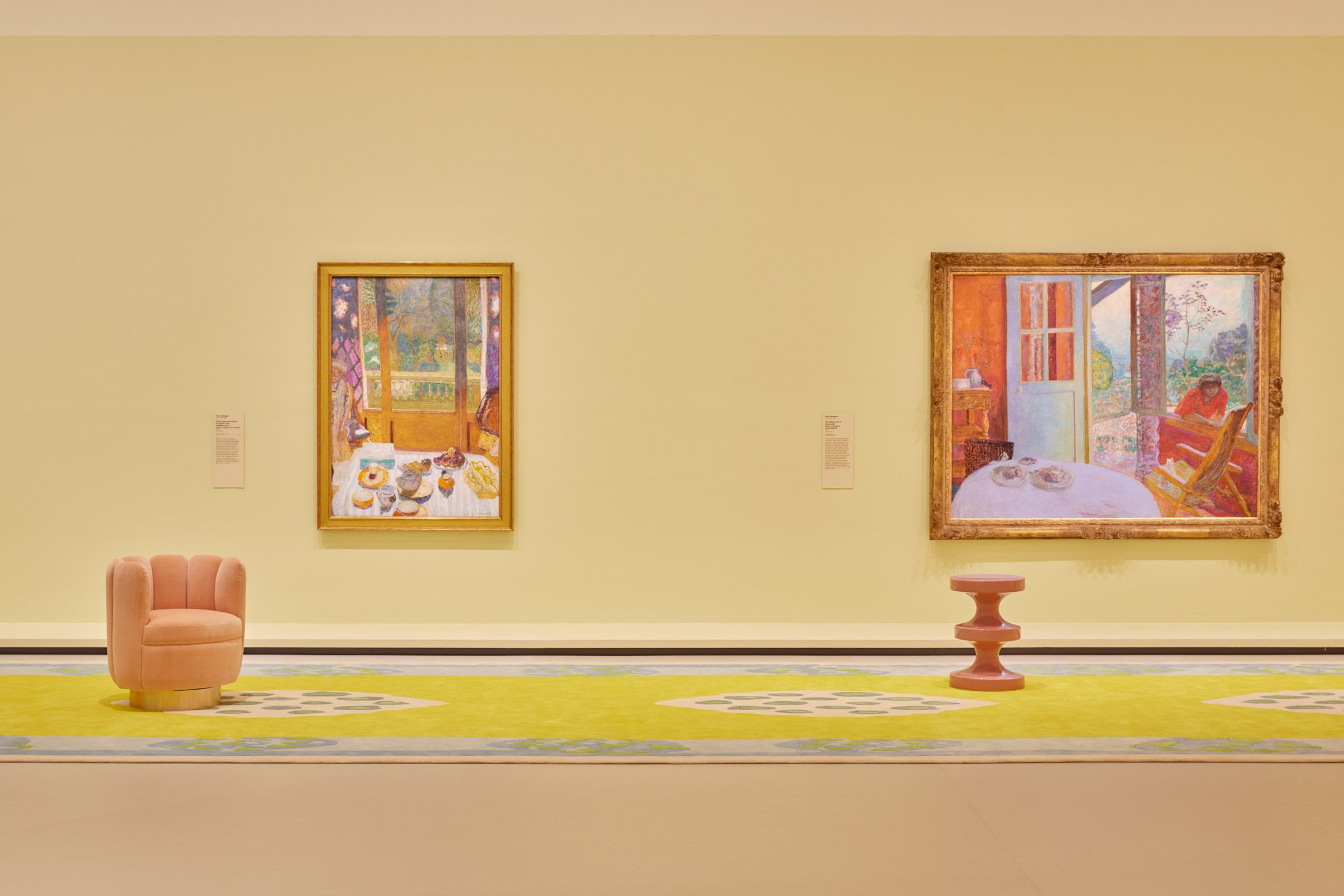 Pale yellow gallery space with two paintings and two stools
