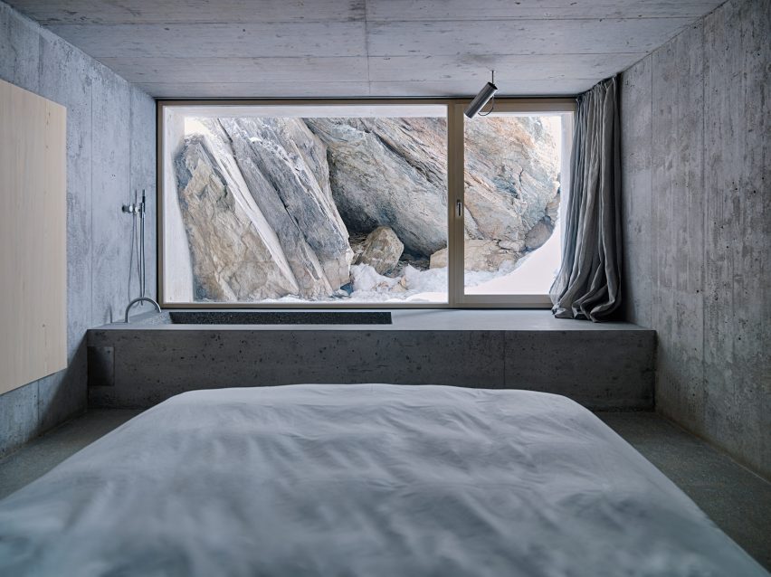 Concrete bedroom with a rectangular bathtub by a window looking out to rocks