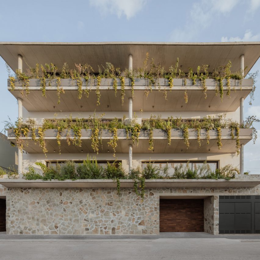 A four-storey apartment building in Mexico with a stone wall and planted balconies