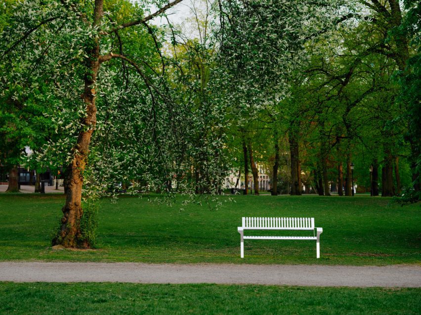 Фотография стальной скамейки Tellus в пышном зеленом общественном парке.