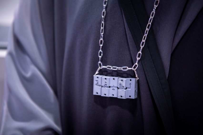 Cinque piccoli cubi incisi su una catena d'argento indossata da una persona vestita di nero