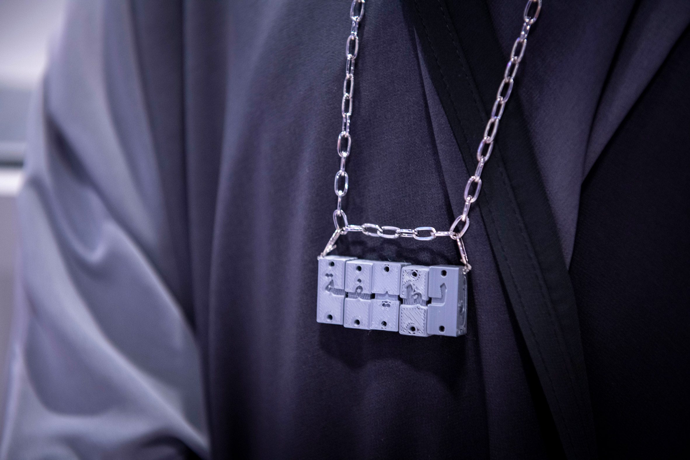 Five small engraved cubes on a silver chain worn by a person in black clothing