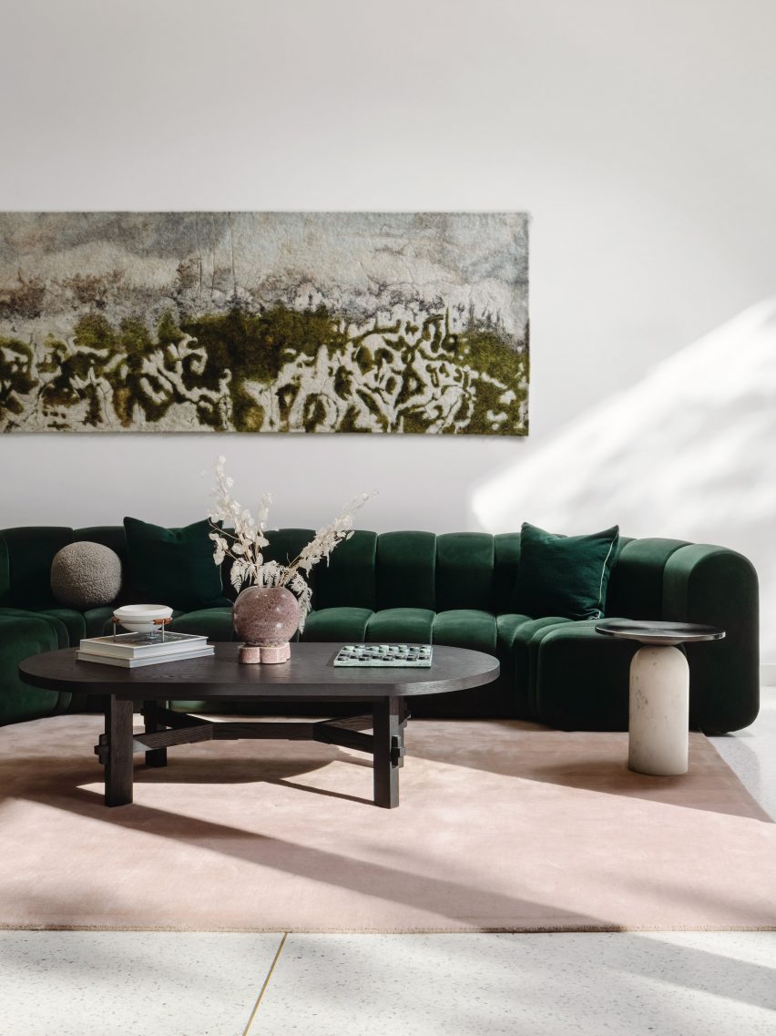 Sofá verde oscuro, alfombra rosa pálido y mesa de centro de madera