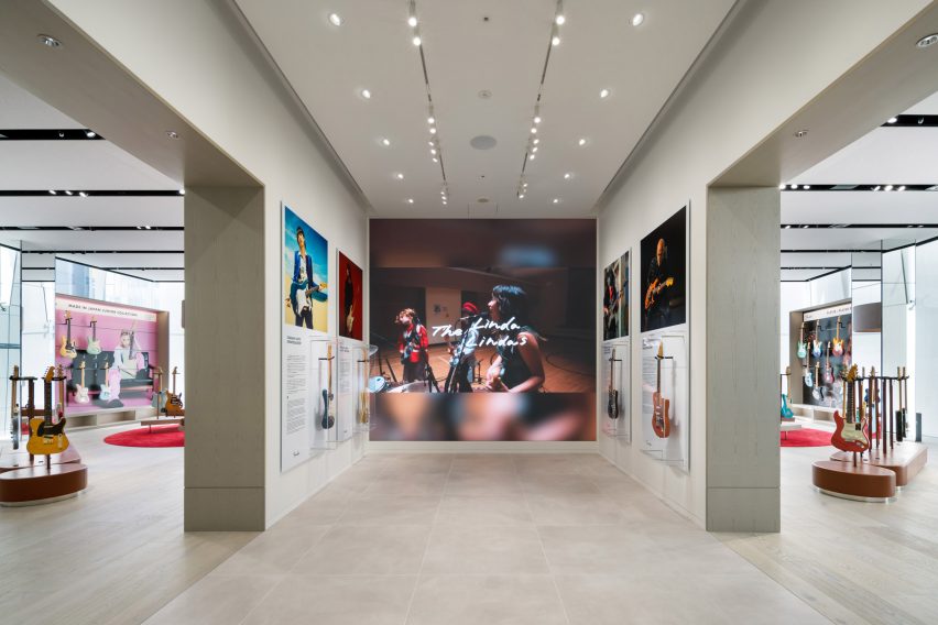 Foto de un espacio similar a una galería que muestra fotos grandes y un video de músicos y sus guitarras, así como guitarras en vitrinas transparentes