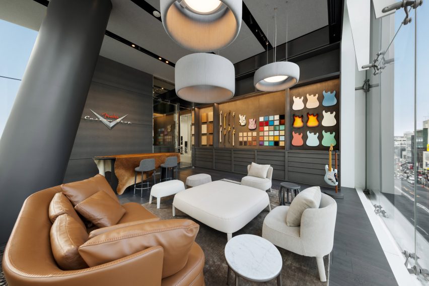 Photo of a dark grey room with big couches and armchairs in the foreground and a library of colourful material and component samples along the back wall. On the side wall, a sign reads Fender Custom Shop
