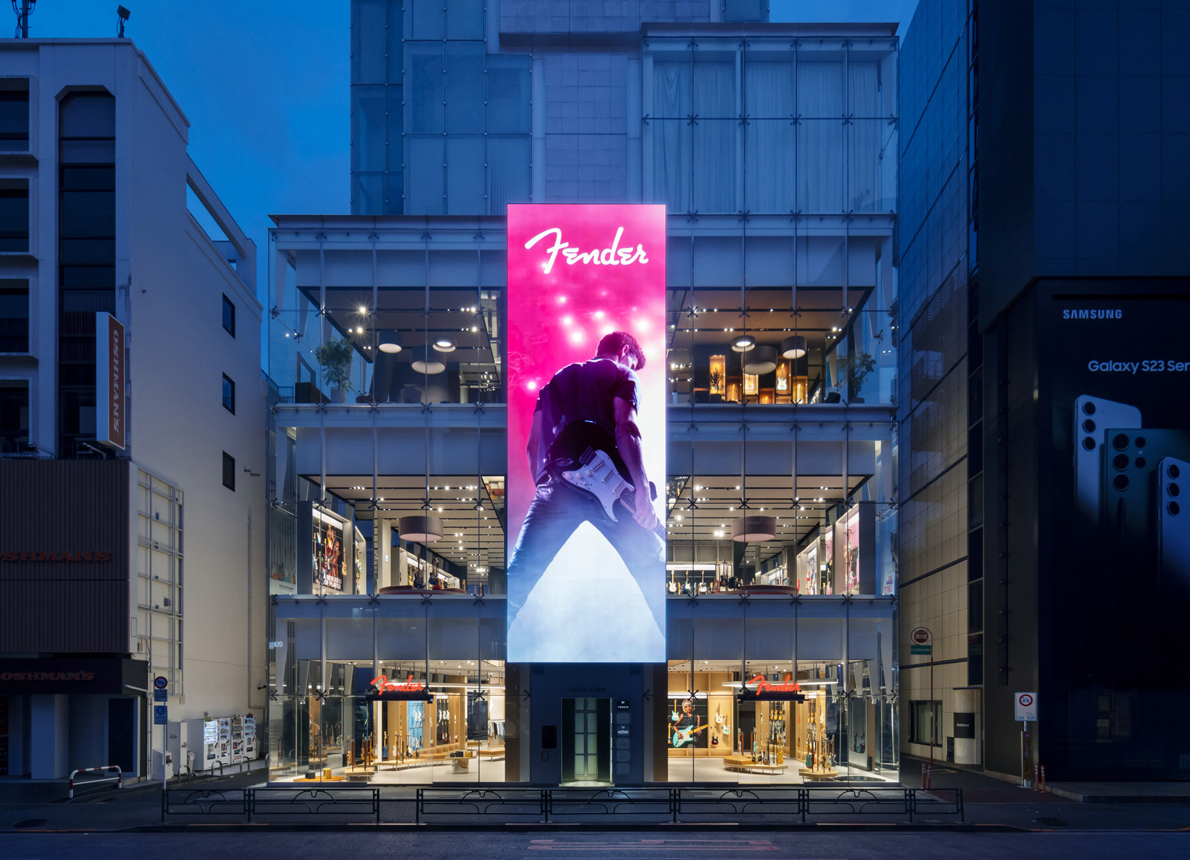 Photo of the exterior of the Fender flagship store, showing the outside of the "Ice Cubes" building in Tokyo with a vertical LED billboard displaying a musician posing with their electric guitar
