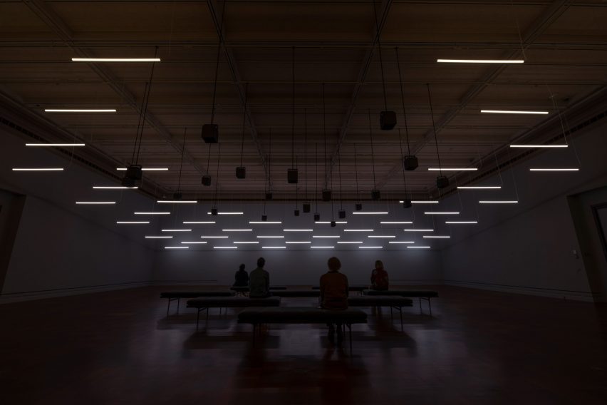 Photo of the Machine Auguries installation at the Toledo Museum of Art, with visitors sitting in a dark room lightly illuminated by overhead lighting