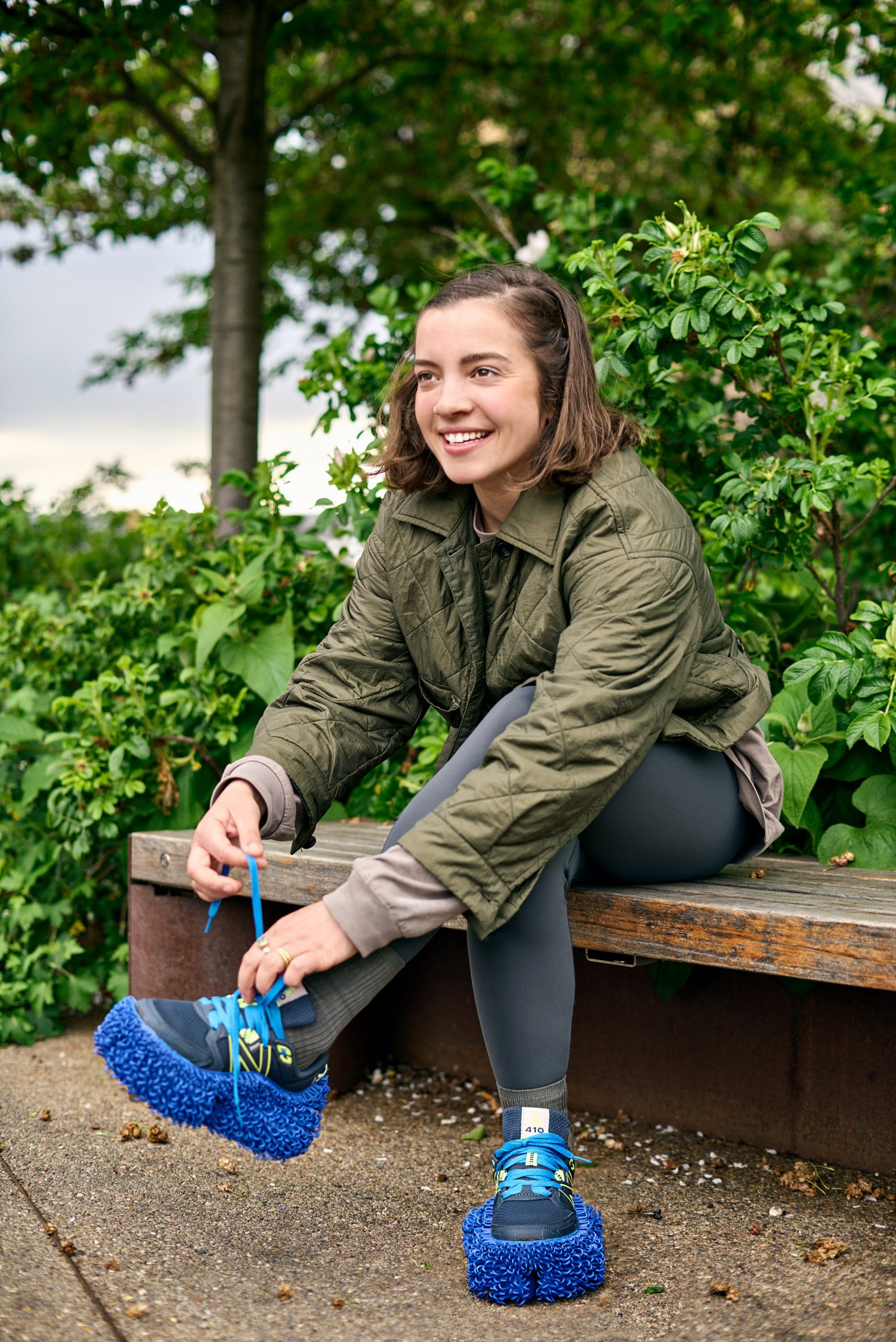 Photo of a young woman sitting on a park bench while she ties the laces on her rewilding trainers