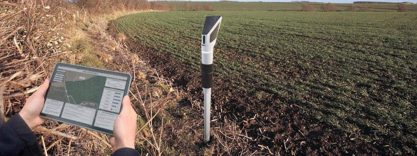 Photograph of gadget in the ground on a field with data showing on a tablet