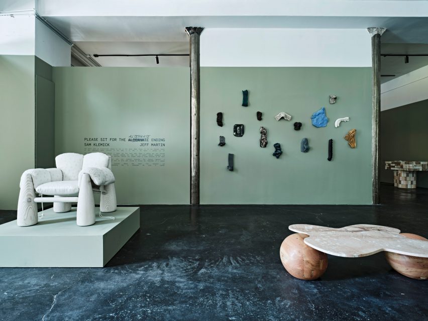 Chair with wooden legs and plush seating in front of green gallery wall