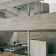 The interior of a concrete home that features a mezzanine and a below-ground kitchen