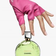 A pink-gloved hand holding a bottle of perfume in a round bottle