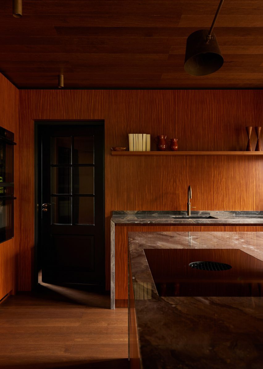 Wood-lined kitchen with a black door and marble worktops