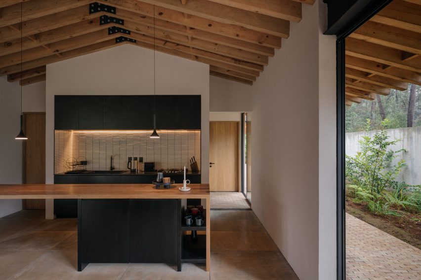 Kitchen in a pitched-roof house with timber roof beams, white walls and timber and black kitchen units