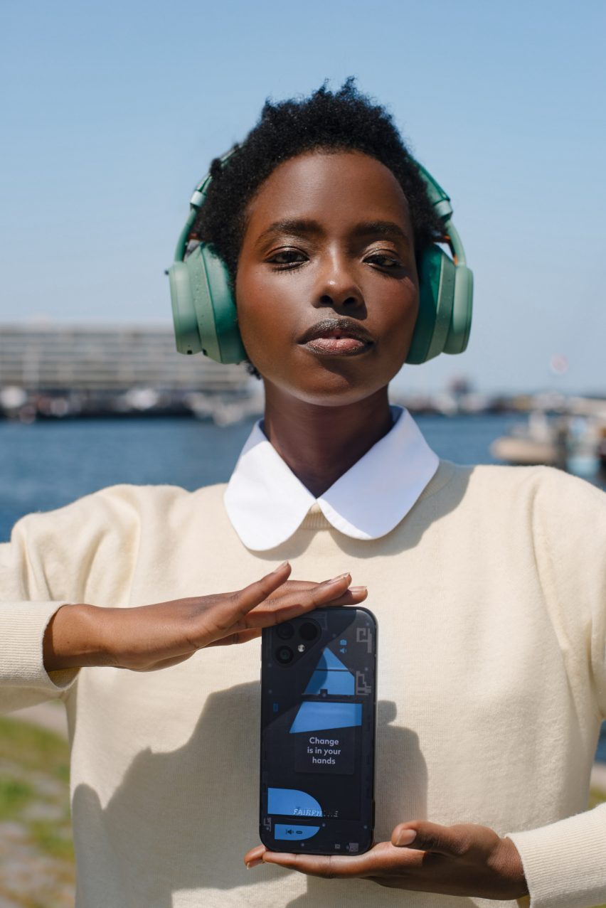 Photo of a young woman wearing headphones and displaying the Fairphone 5 in the Transparent Edition, showing the blue shapes of different modules under the surface