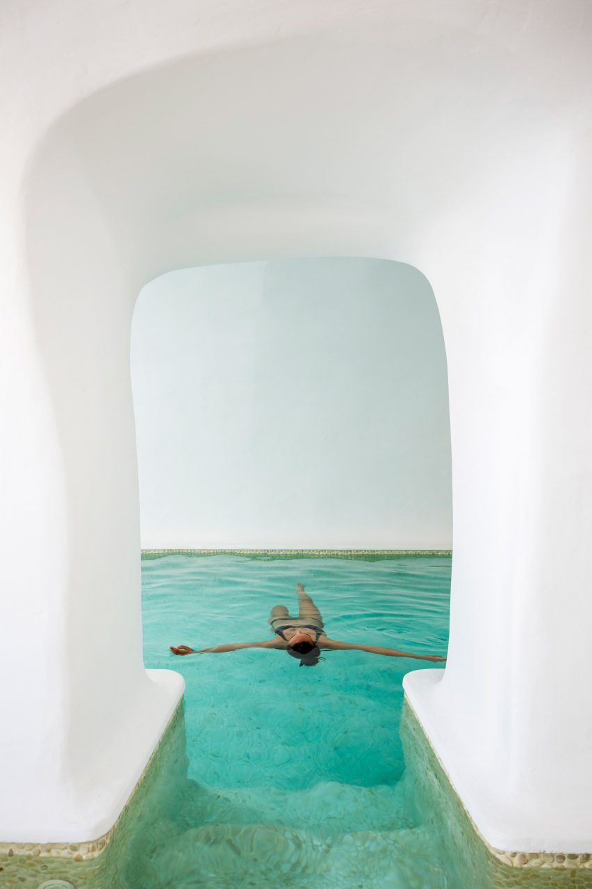 Woman floating in pool framed by white walls
