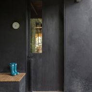 A black door with a bench next to it that has little blue rain boots