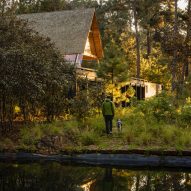 A man and dog walking toward an elevated a-frame home in the forest
