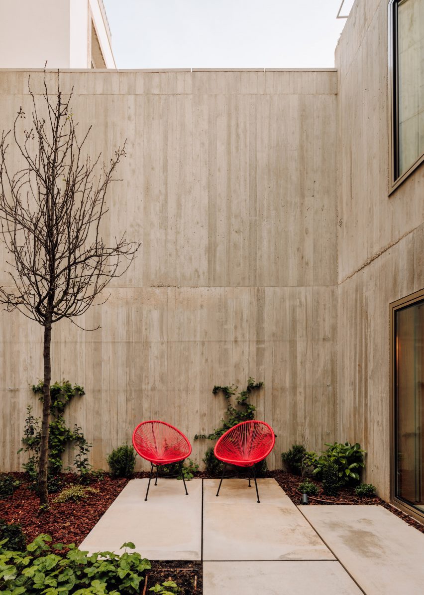 Residential courtyard in a concrete home with planting and red chairs