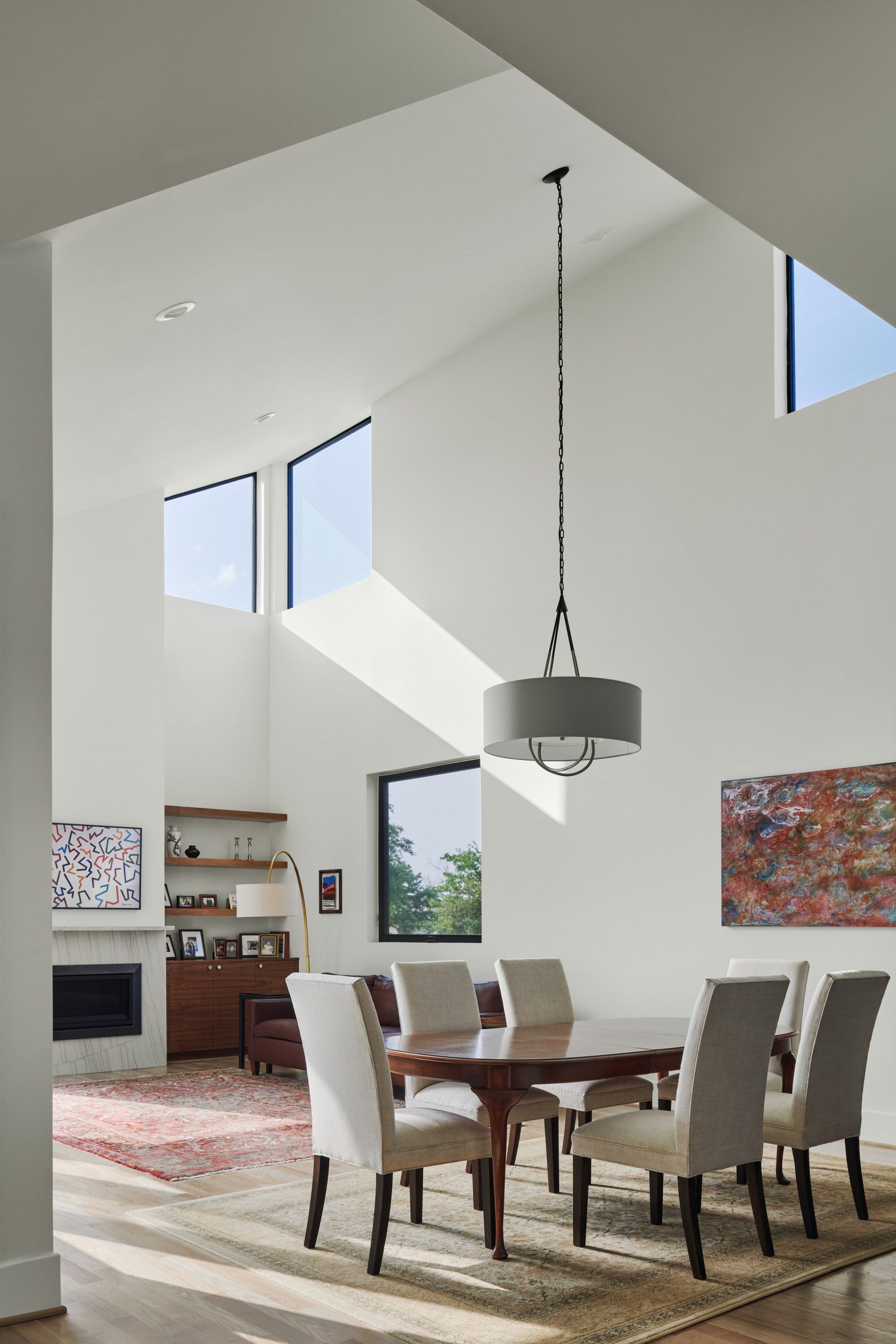 White double-height dining room with high-level windows and pendant light over a table